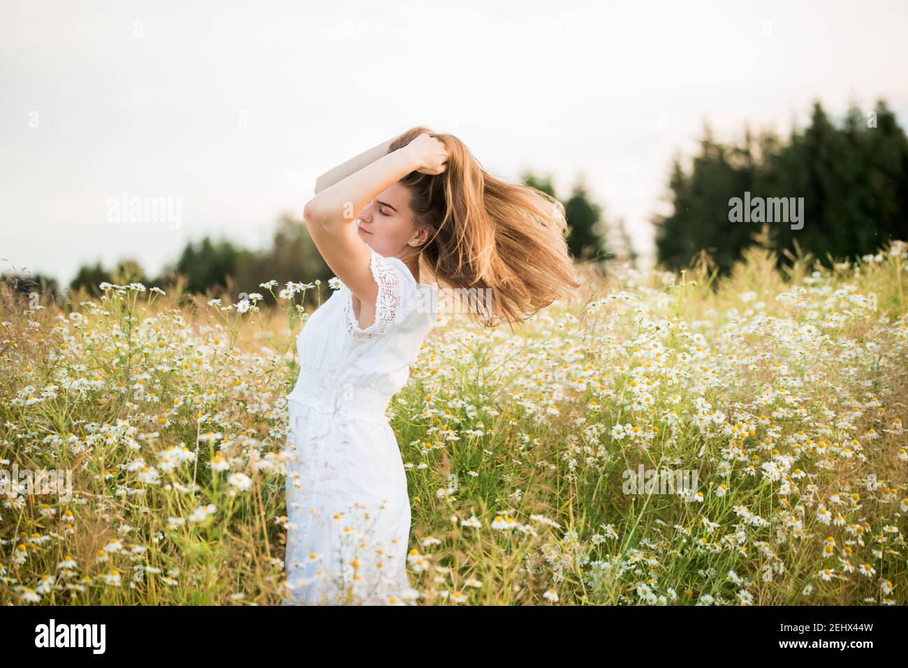 Happy girl on the camomile field, summer sunset. in a white dress. running and spinning, the wind in my hair, life style. freedom concept and hot Stock Photo