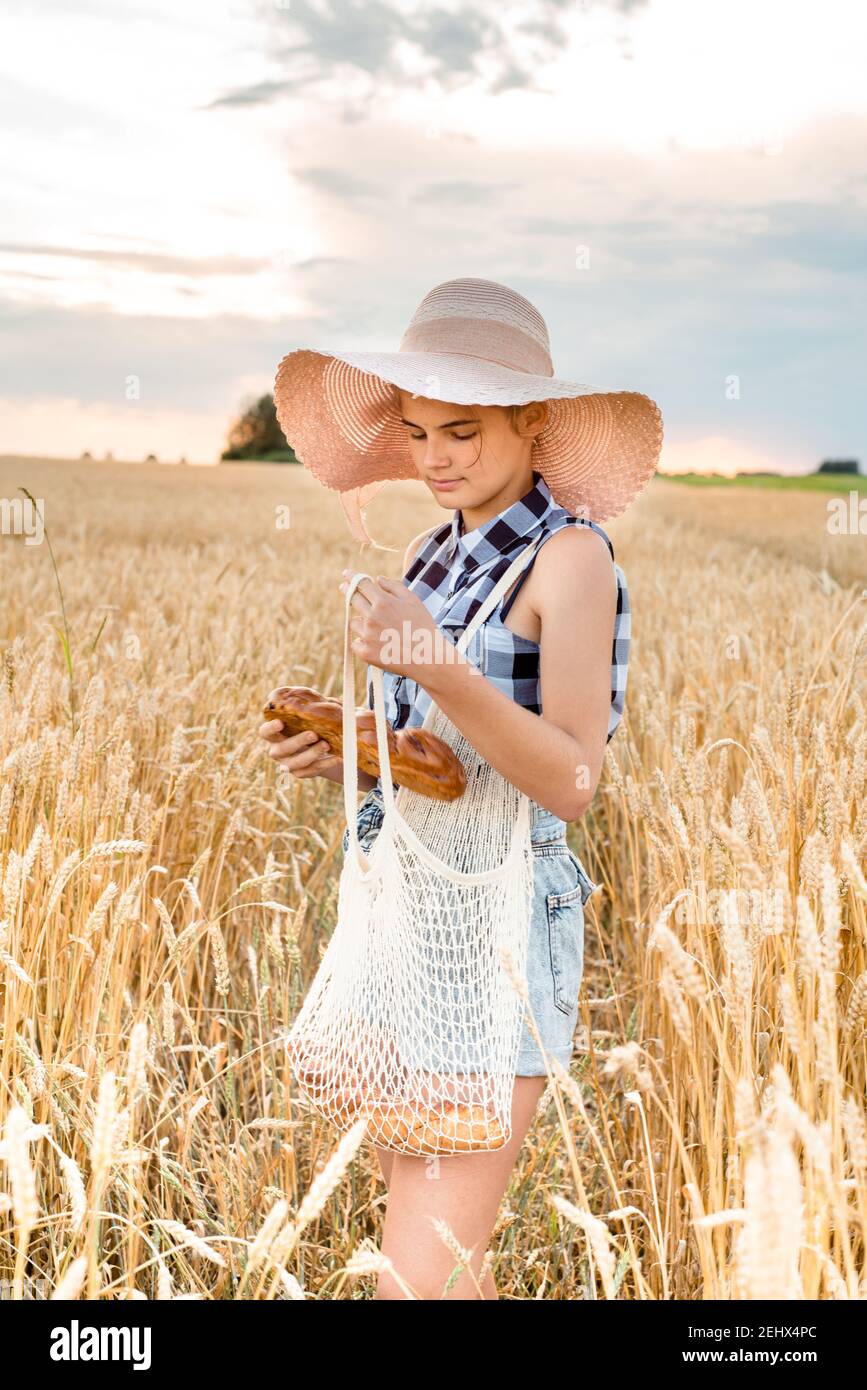 Happy girl walking in golden wheat,with her back, outdoor lifestyle. Freedom concept. Cute little girl in summer field.takes bread from an eco bag Stock Photo
