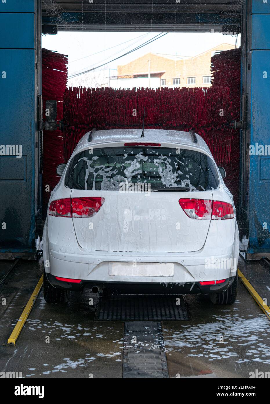 white car washing in automatic car wash with red rollers and lots of soap Stock Photo