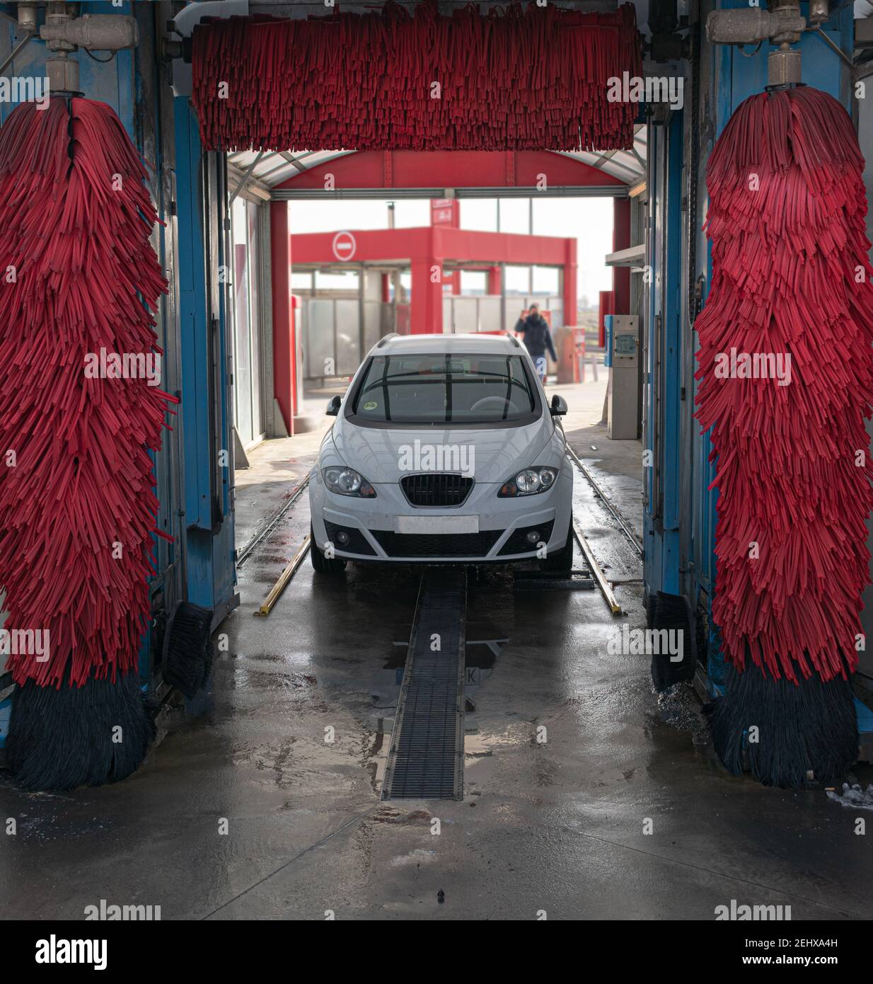 white car washing in automatic car wash with red rollers and lots of