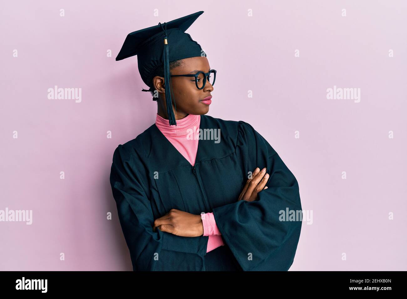 Young african american girl wearing graduation cap and ceremony robe looking to the side with arms crossed convinced and confident Stock Photo