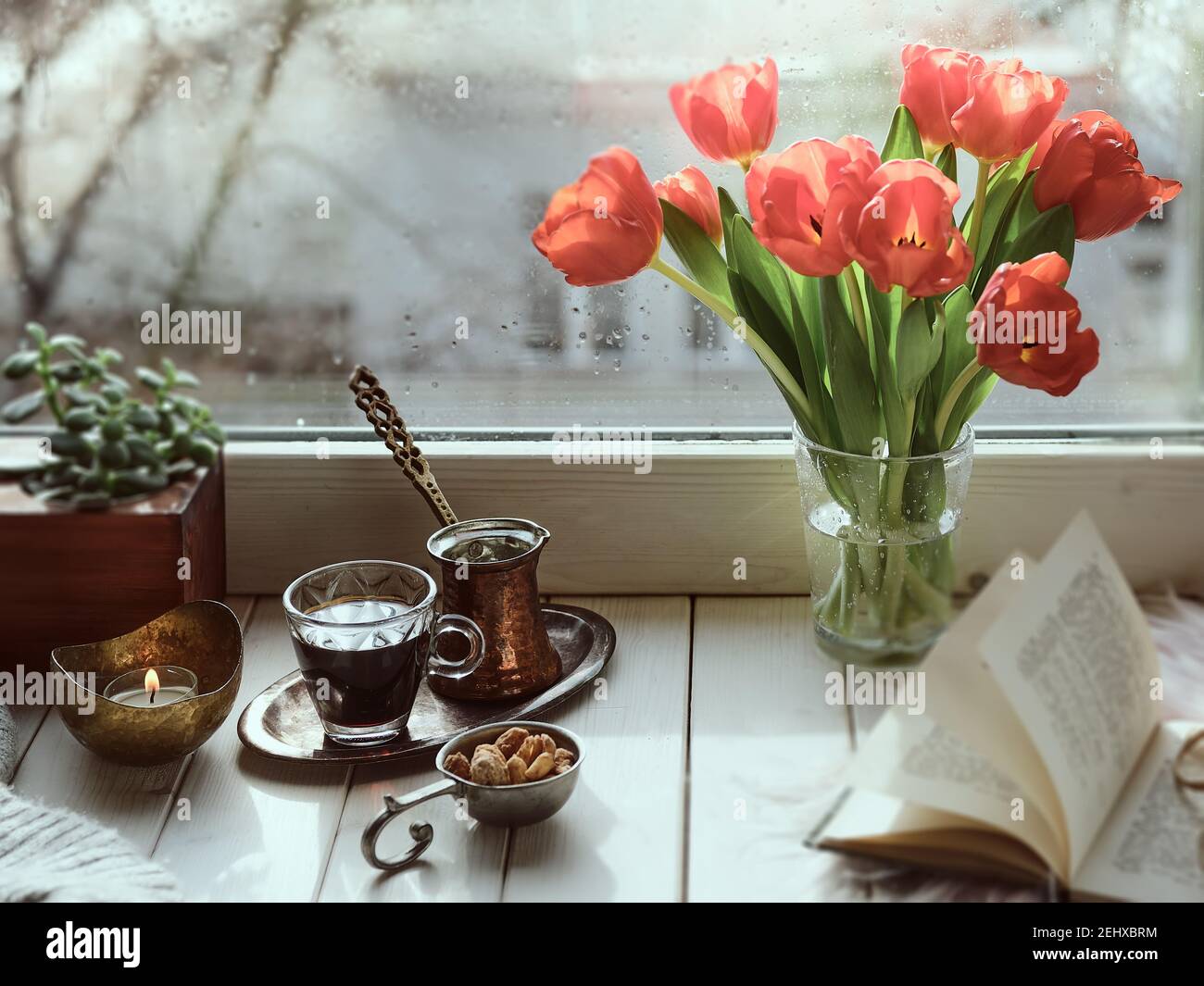 Oriental coffee cooked in traditional Turkish copper coffee pot with flowers on window sill. Wooden windowsill with bunch of tulips book.Cozy scene, h Stock Photo