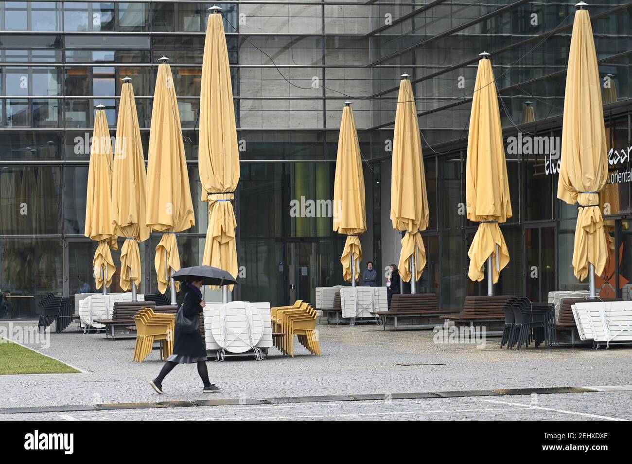 Topic picture: Coronavirus pandemic/consequences for gastronomy: stacked chairs and tables on February 19th, 2021 in Munich - a passer-by with an umbrella walks past. | usage worldwide Stock Photo