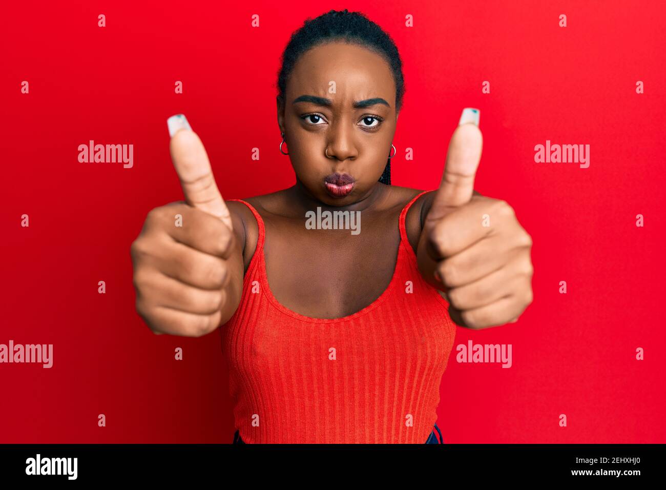 Young african american woman doing thumbs up positive gesture puffing cheeks with funny face. mouth inflated with air, catching air. Stock Photo