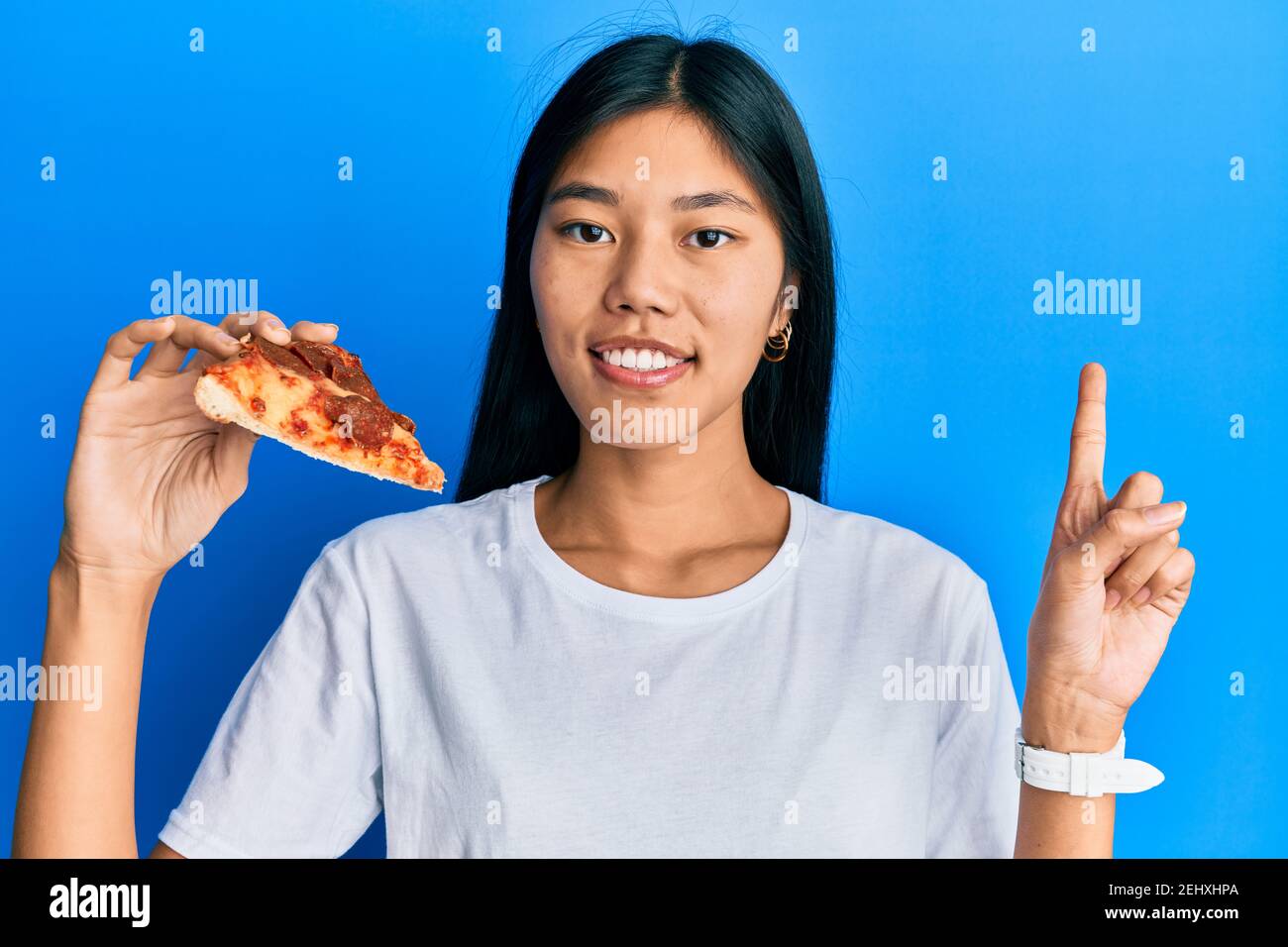 Young chinese woman eating tasty pepperoni pizza surprised with an idea