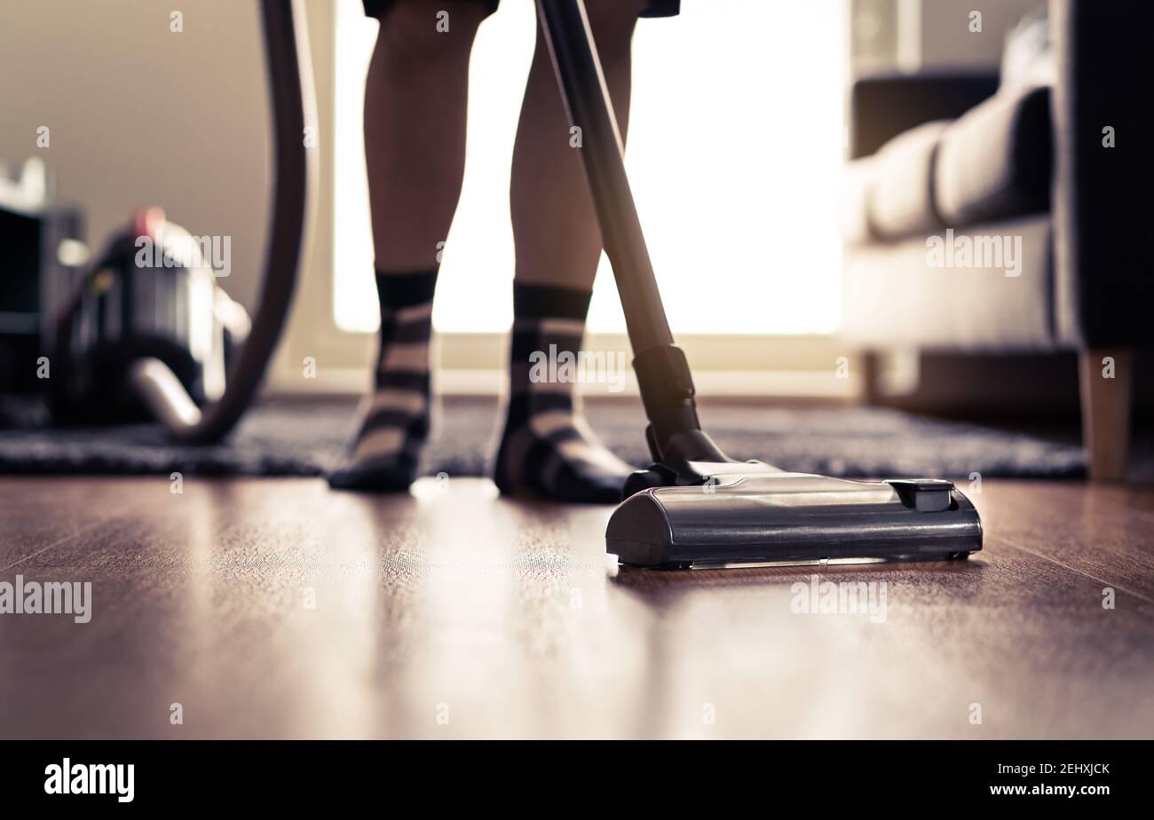 Vacuum cleaner. Man cleaning floor at home and doing household chores in modern apartment. Sun light from window. Happy person vacuuming living room. Stock Photo
