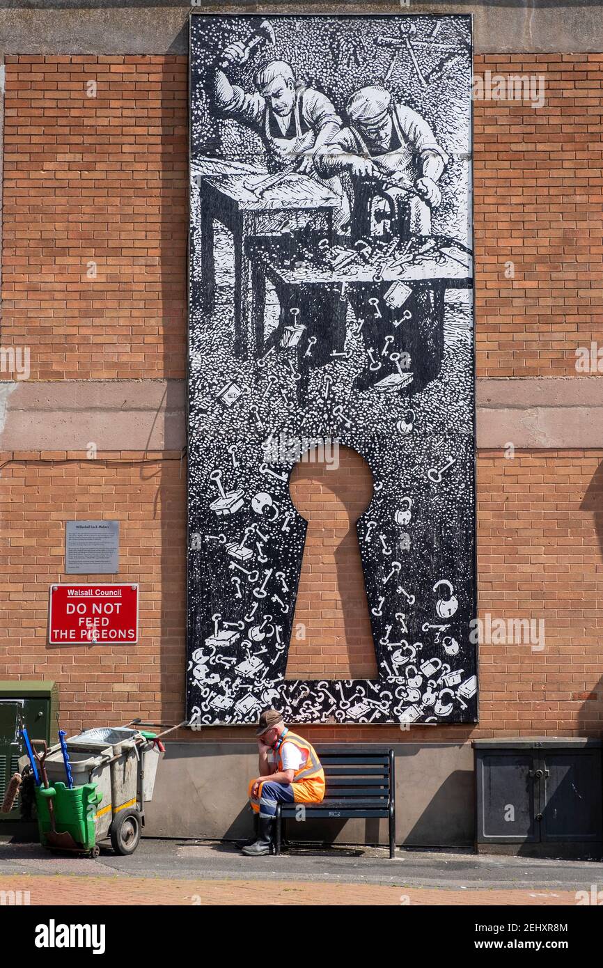 Street cleaner sits in from of lock makers's mural, tribute to people of town, Willenhall, West Midlands Stock Photo