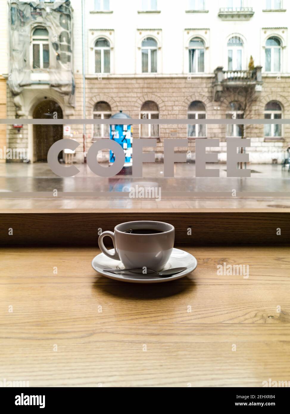 Small white coffee cup in cafe in front of window with coffee word