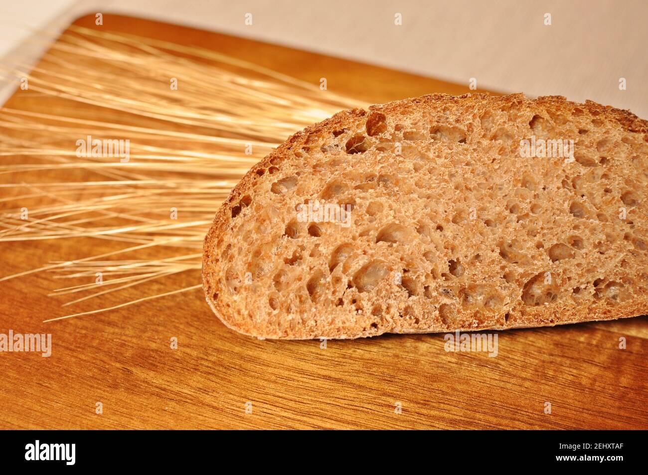 One cereal brown slice, with dried wheat decoration on wooden table background. Front view, copy text Stock Photo