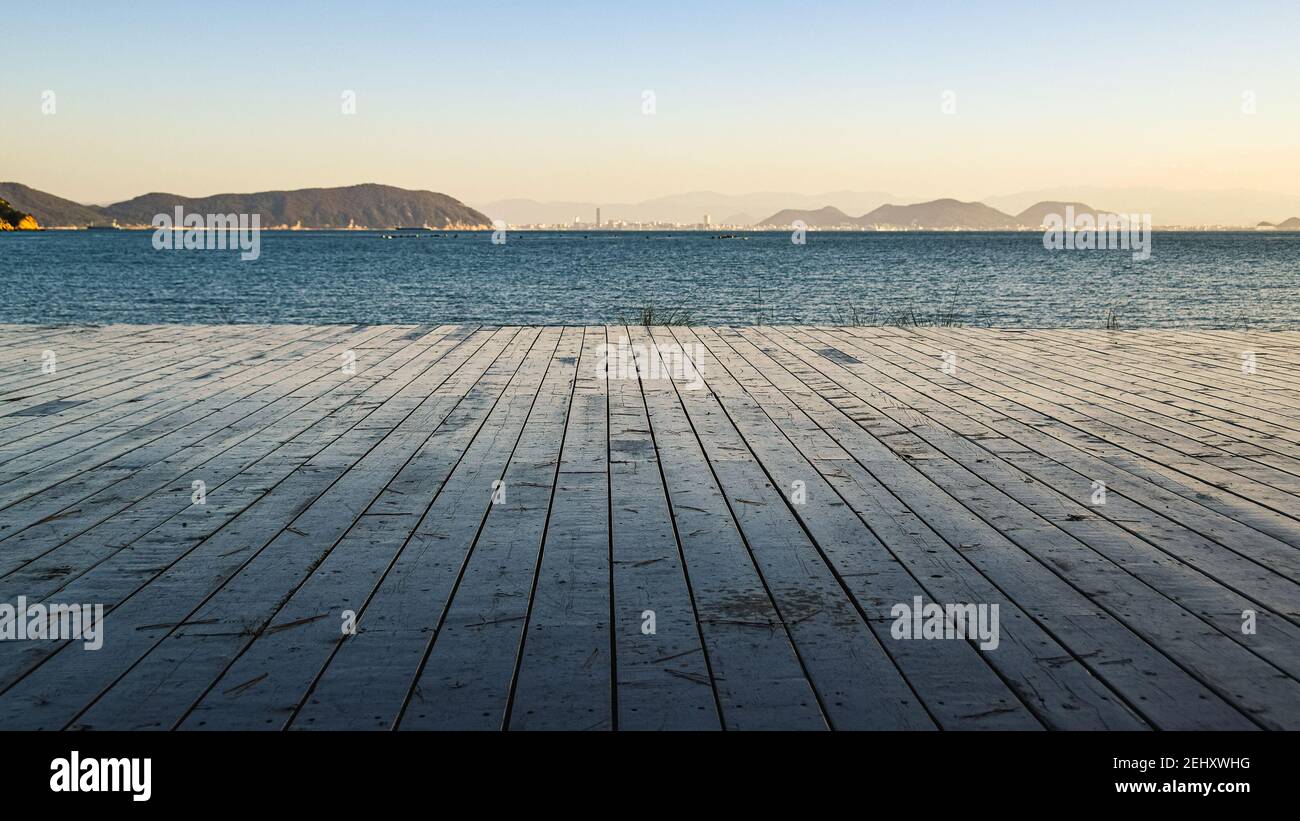 View towards the sea from the wooden deck with two pine trees on the shore of Naoshima Island, Japan, durinng misty sunset with the Great Seto Bridge Stock Photo