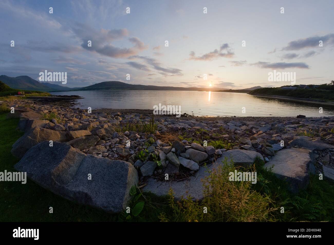 A rocky boulder sea shore at sunset. Looking west near East Suisnish on the Isle of Raasay, isle of skye in the distance. A fish eye perspective. Stock Photo