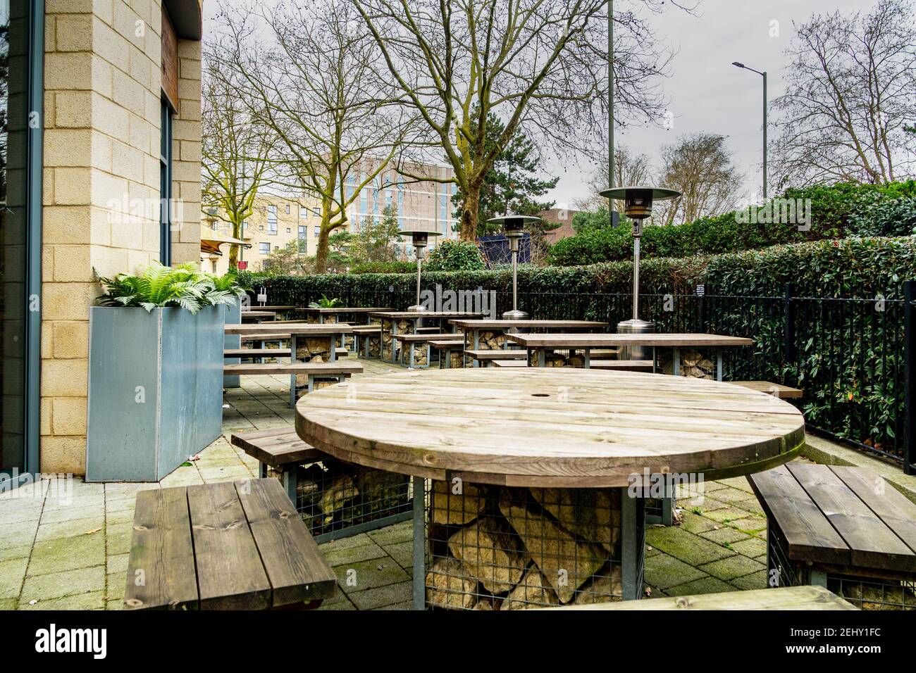 An empty pub beer garden during the covid19 lockdown in London, UK. Patio heaters and wooden bench and tables surrounded by green plants. Stock Photo