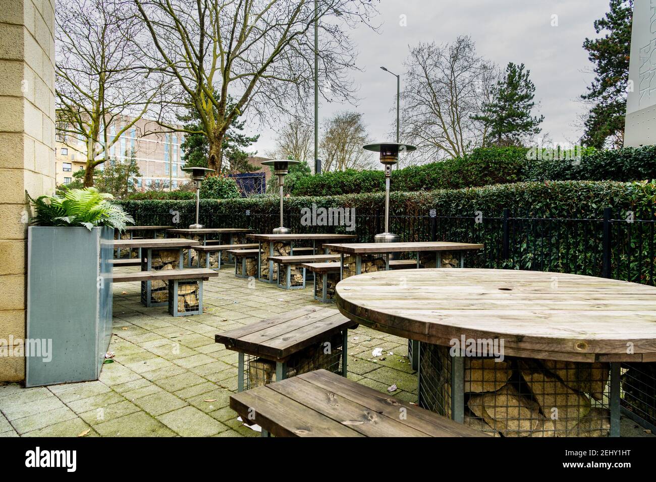 An empty pub beer garden during the covid19 lockdown in London, UK. Patio heaters and wooden bench and tables surrounded by green plants. Stock Photo