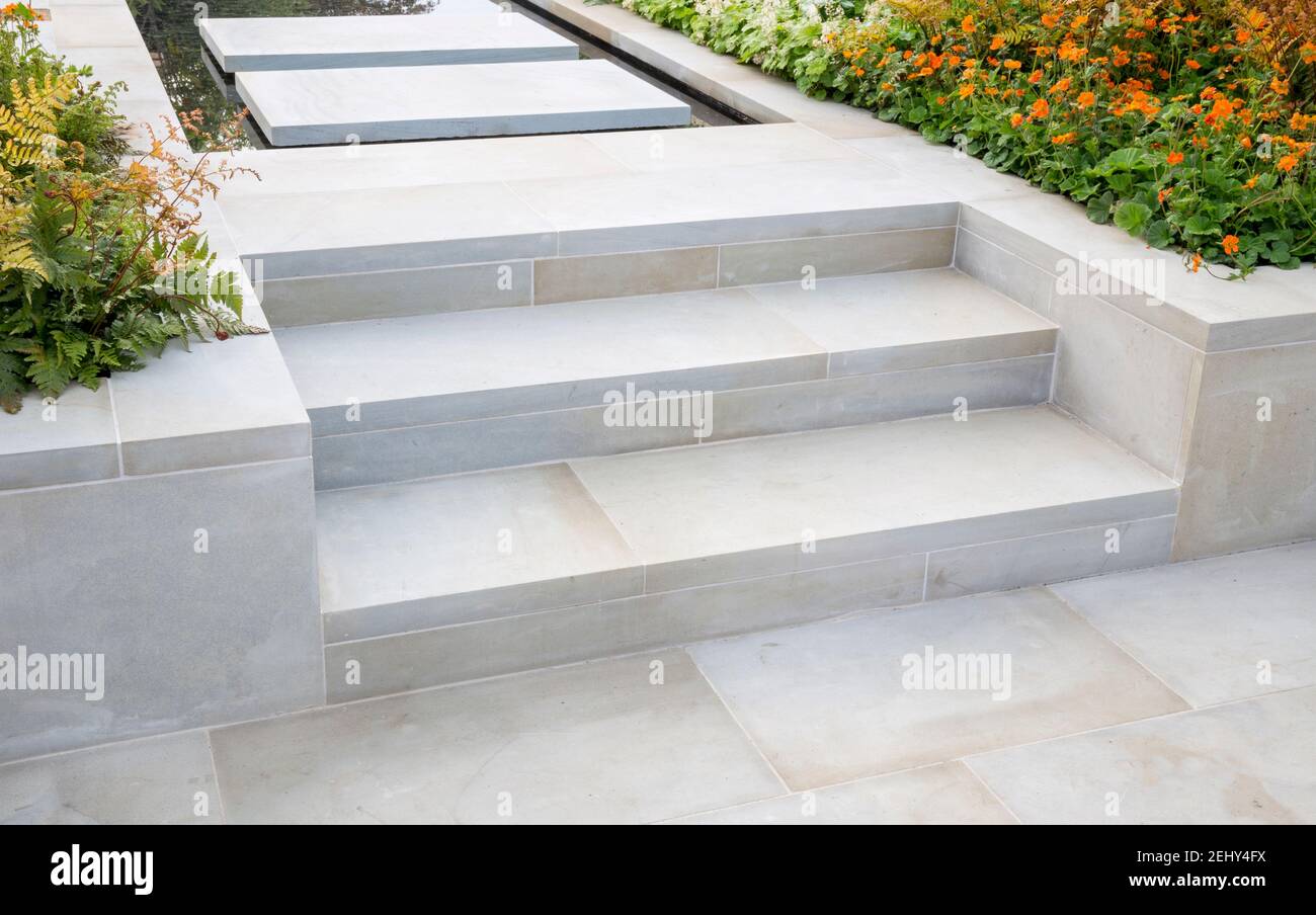 Large Yorkstone steps leading up to floating stepping stone slabs patio over a water feature pool - borders planted with ferns and Geum Borisii  UK Stock Photo