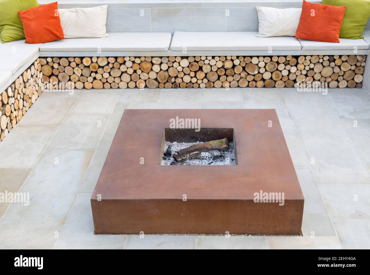 Yorkstone stone sunken garden patio with corten steel fire pit firepit garden bench seat with colourful cushions insect habitat log storage England UK Stock Photo