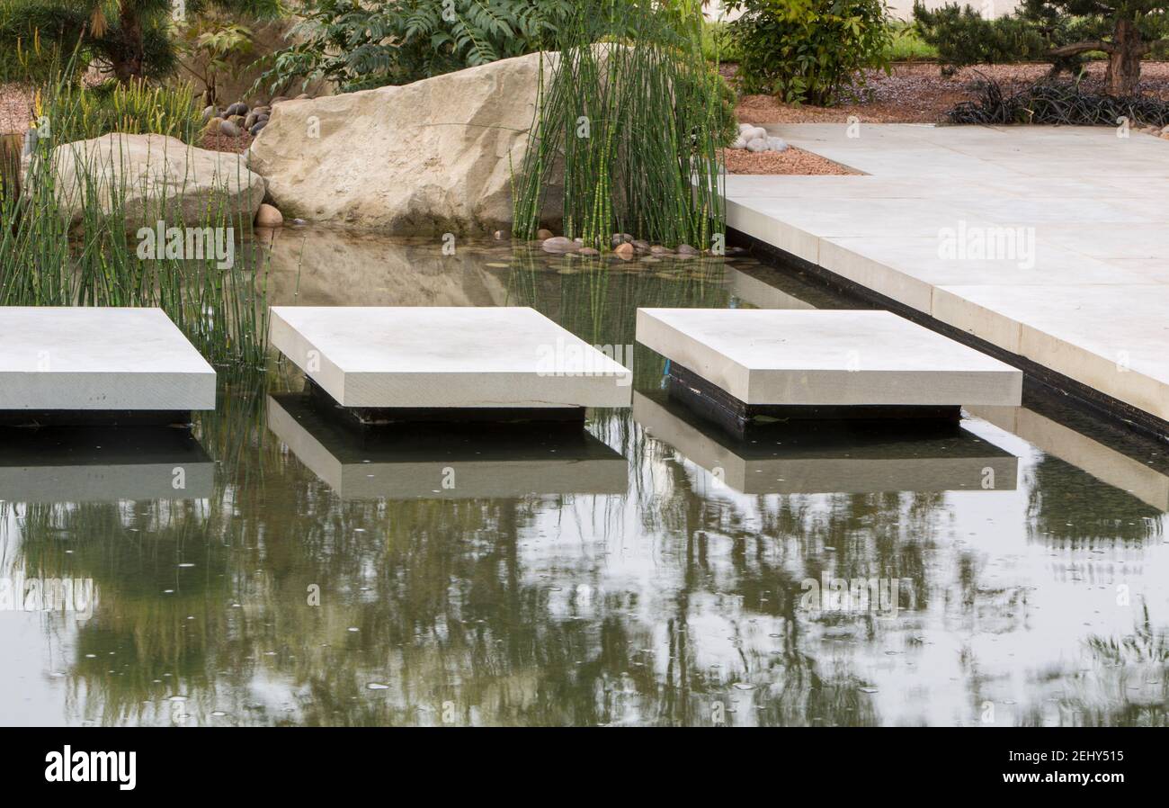 Floating stone stepping stones over a pond water feature planted with Equisetum hyemale Stock Photo