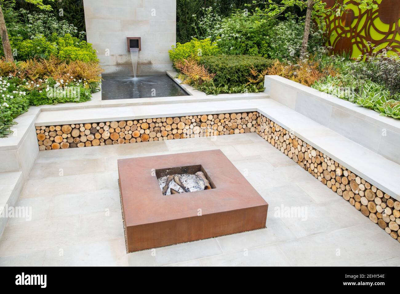 Sunken garden stone patio with corten steel firepit fire pit raised beds and water feature and garden bench with log storage underneath UK Stock Photo