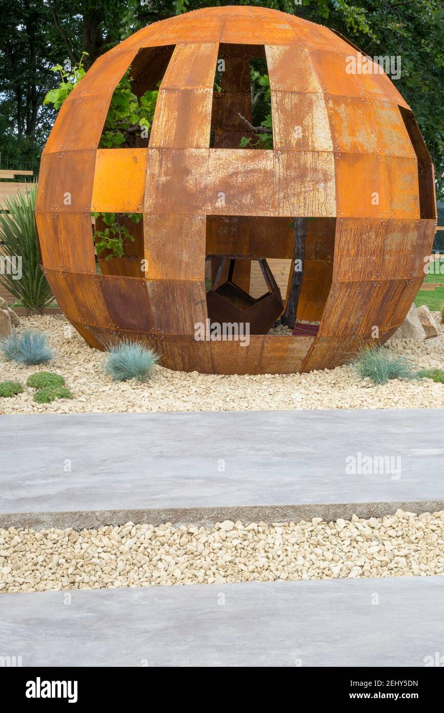 A corten steel rusted steel pod structure with a gravel bed garden planted with grasses and large giant stone paving slabs England GB UK Stock Photo