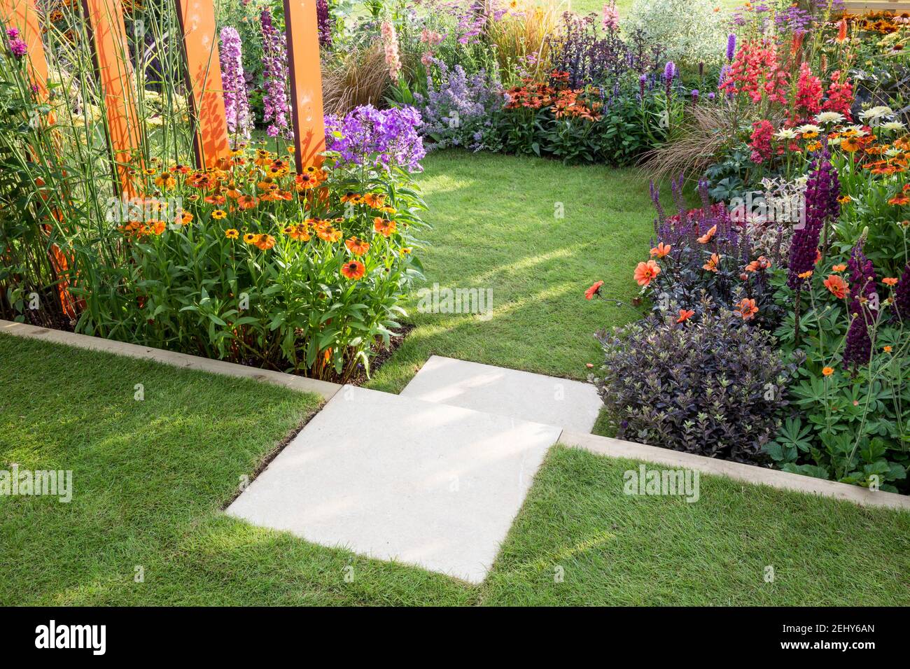 A small size garden - stone steps leading to a lawn grass area with flowerbeds filled with flowers plants including Helenium - Dahlias England GB UK Stock Photo