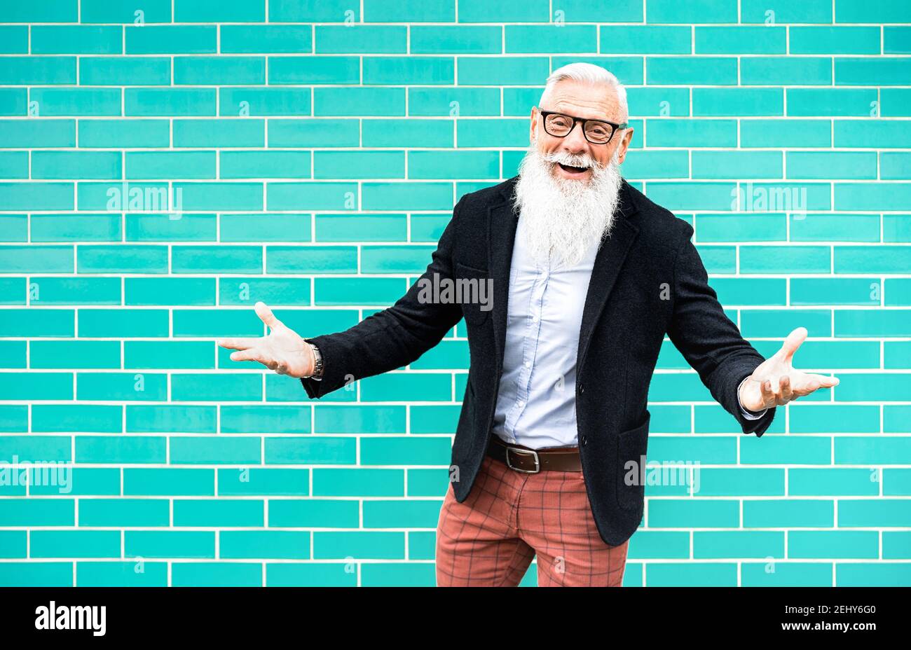 Cheerful hipster man on welcome mood posing against turquoise wall background - Trendy old person wearing casual fashion clothes - Happy elderly life Stock Photo