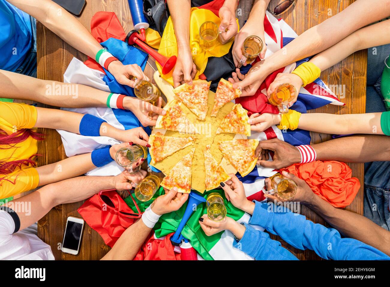 Top view of multiethnic hands of football sport supporter sharing pizza margherita - Friendship concept with soccer fans enjoying food together Stock Photo