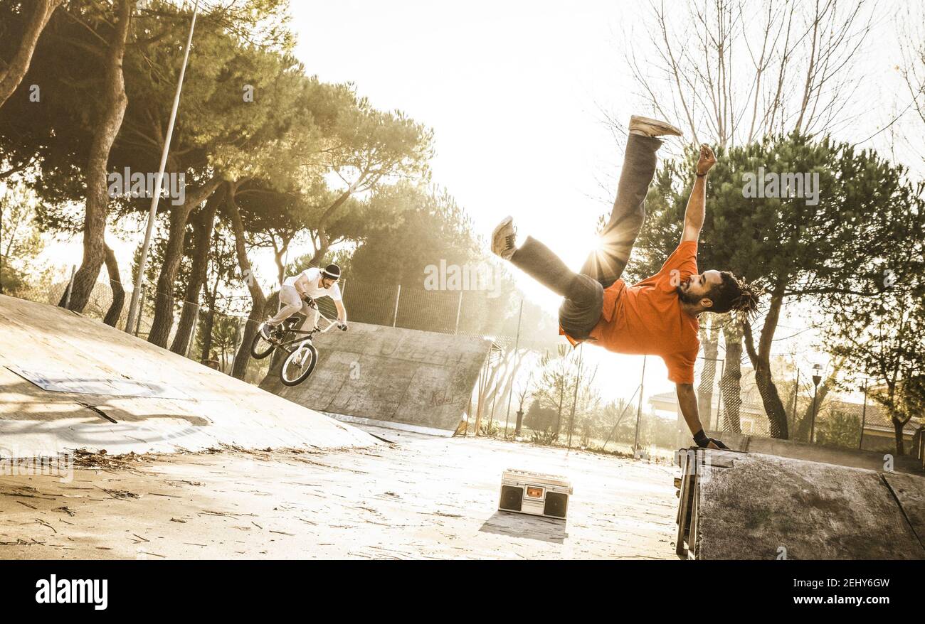 Urban athlete breakdancer performing acrobatic jump flip at skate park - Guy riding bmx bicycle behind mate acrobat dancing with extreme move Stock Photo