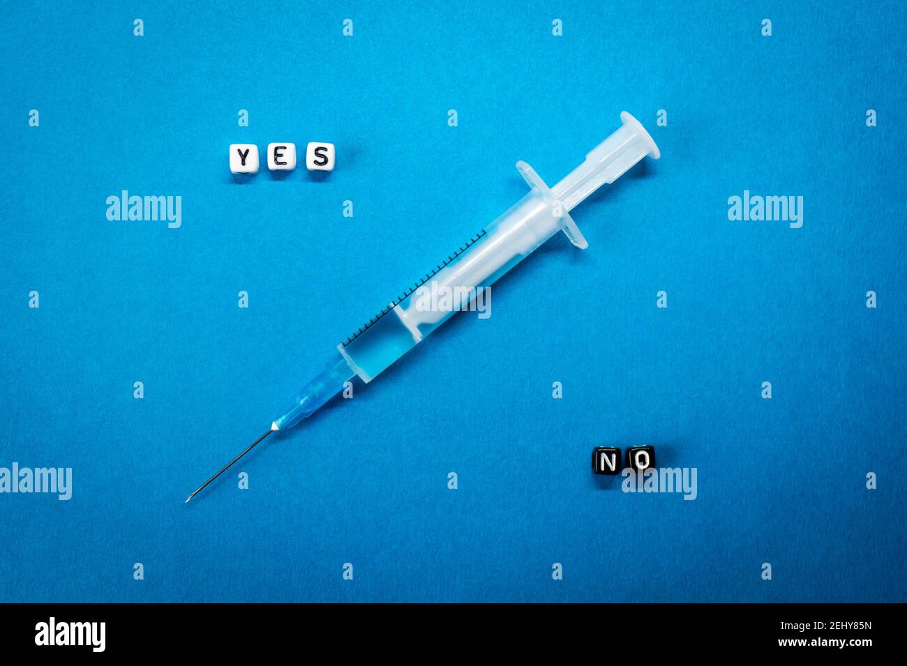 Yes No words made of square letters and a syringe on blue background. Pros and cons of coronavirus vaccine, concerns and doubts about vaccination Stock Photo