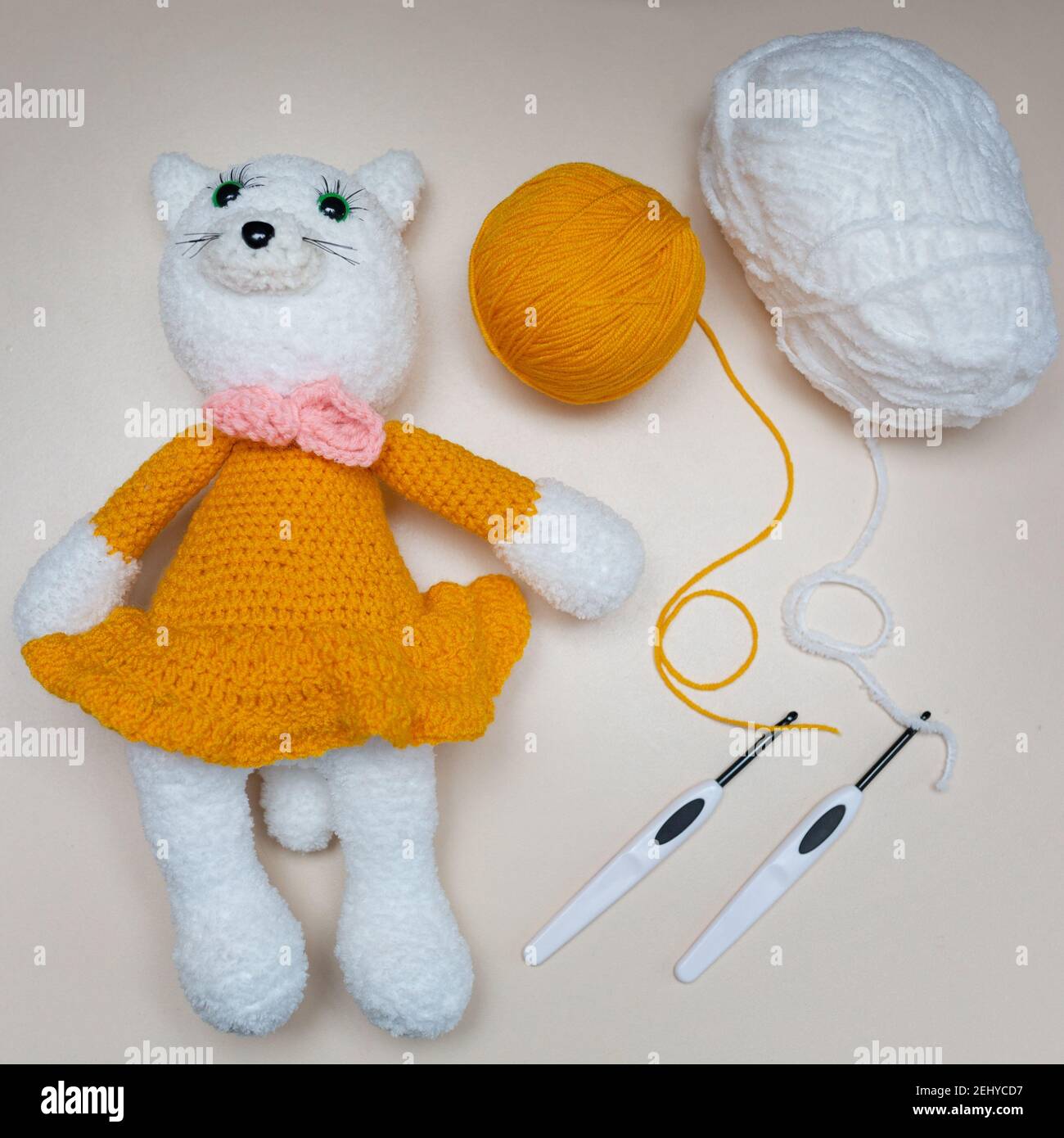 Handmade knitted toy. Toy white mouse in an orange skirt with knitting needles on a gray background. Crocheted stuffed animals. Stock Photo