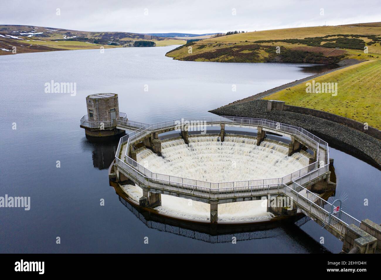 East Lothian, Scotland, UK. 20 Feb 2021. Meltwater from recent snow and heavy rain has filled Scottish reservoirs to capacity. Dam spillways are now full whilst discharging water downstream. Pic; Drone image of circular siphon spillway at Whiteadder Dam running at full capacity to discharge water from the reservoir. Iain Masterton/Alamy Live News Stock Photo