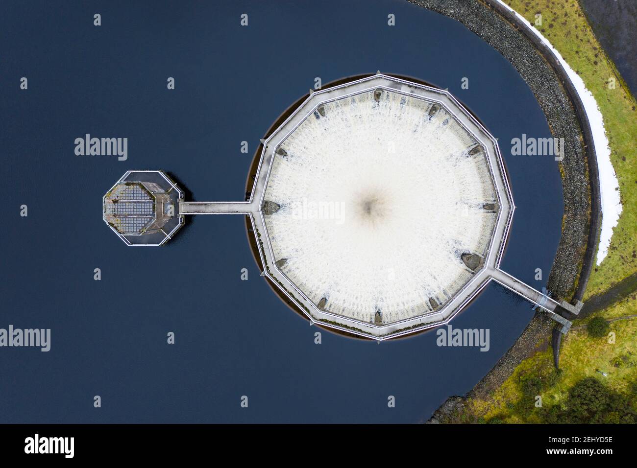East Lothian, Scotland, UK. 20 Feb 2021. Meltwater from recent snow and heavy rain has filled Scottish reservoirs to capacity. Dam spillways are now full whilst discharging water downstream. Pic; Drone image of circular siphon spillway at Whiteadder Dam running at full capacity to discharge water from the reservoir. Iain Masterton/Alamy Live News Stock Photo