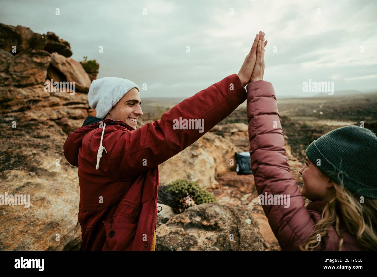 Caucasian couple high five reaching top of mounting hiking at sunset Stock Photo