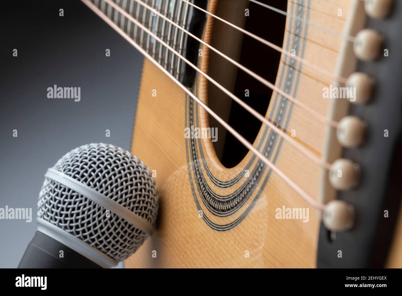 microphone leaning on the body of an acoustic guitar with gray background Stock Photo