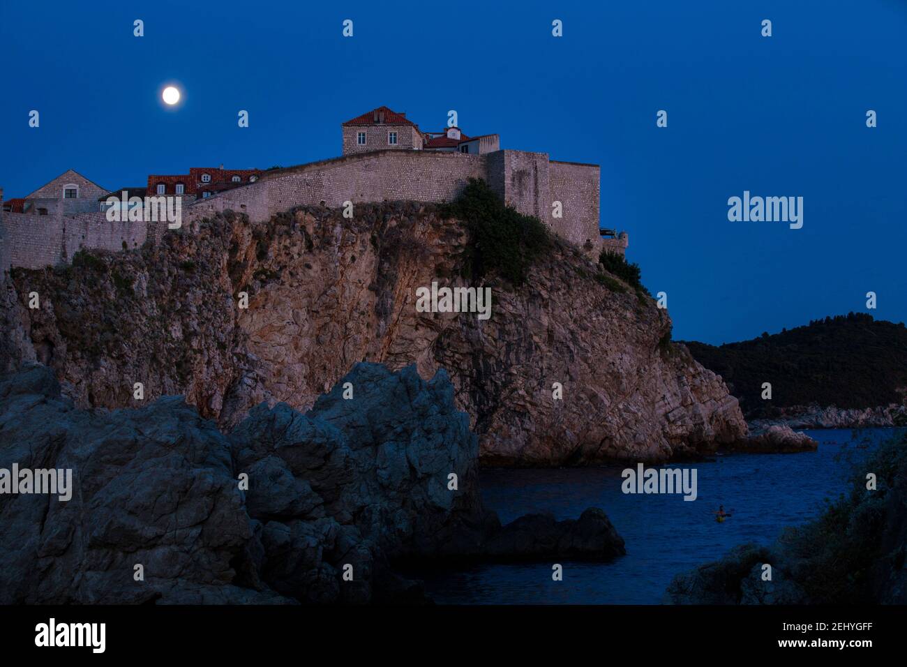 Night Photograph of City of Dubrovniks Walls on a Cliff with a Full Moon and Sea in the background Stock Photo