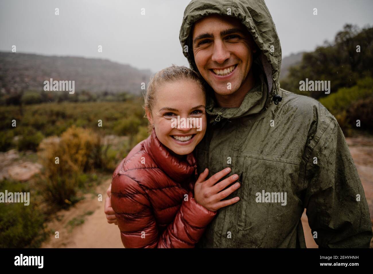 Happy smiling couple resting after steep trail run up gravel mountain slope in cold cloudy weather with rain jackets Stock Photo