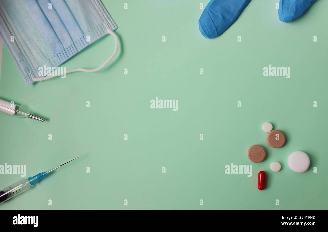 Medical flatlay on a green background. Pills, mask syringe and thermometer. Stock Photo