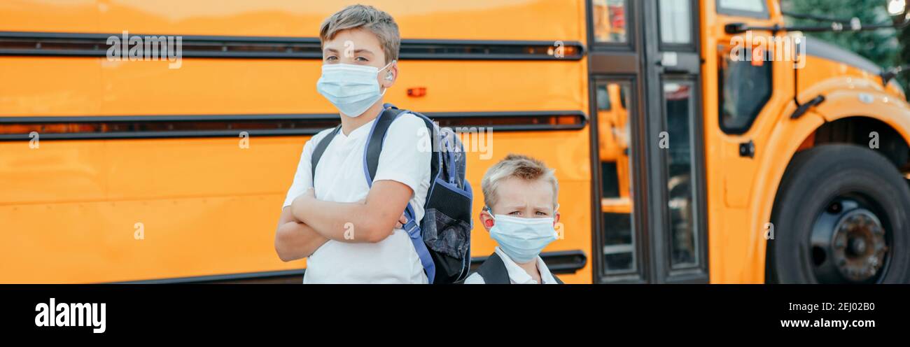 Brothers students kids wearing face mask near yellow bus. Education and back to school in September. New normal at coronavirus covid-19. Web banner Stock Photo