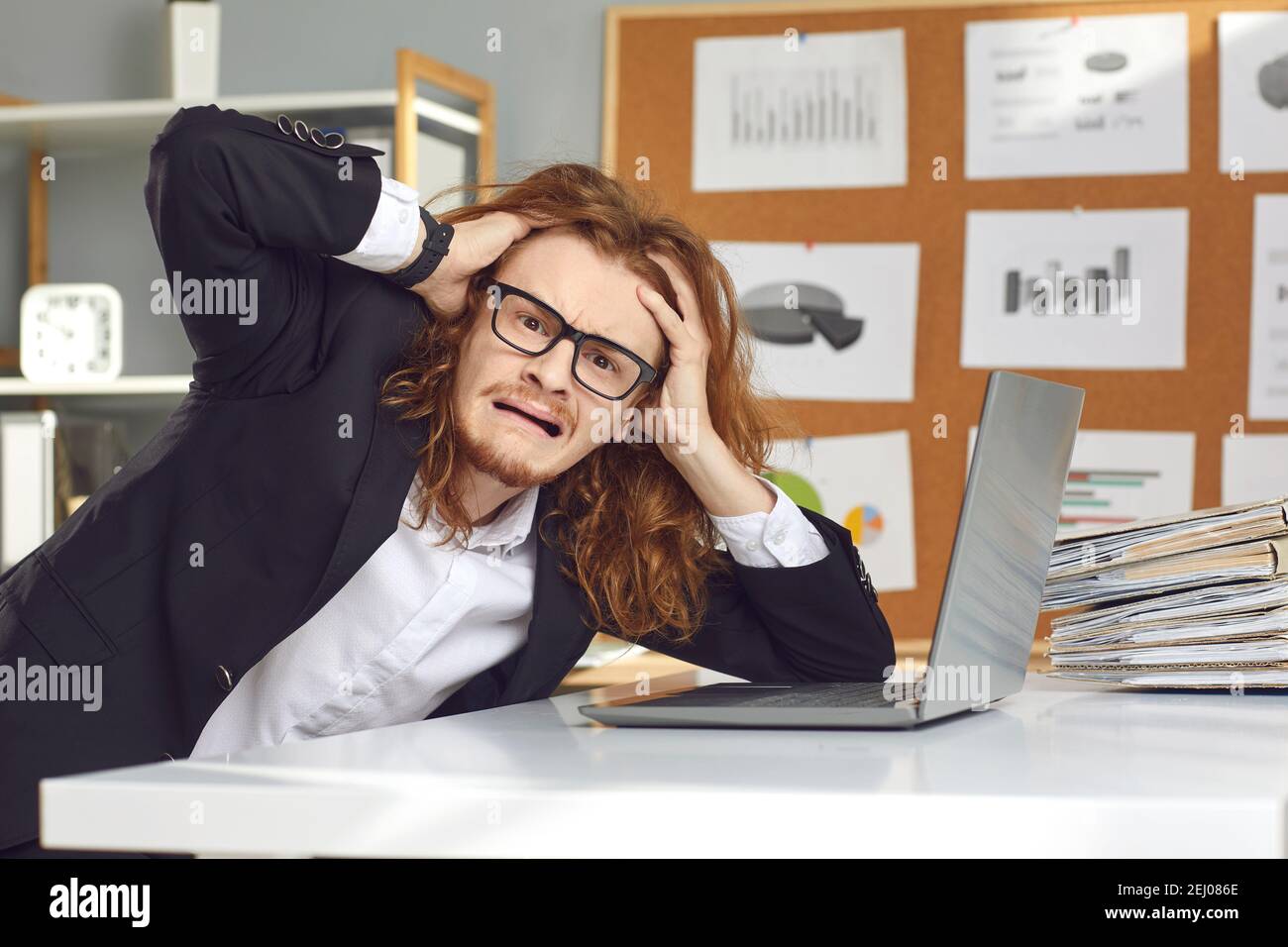 Funny young weird stressed man accountant sitting at laptop touching head feeling burnout Stock Photo