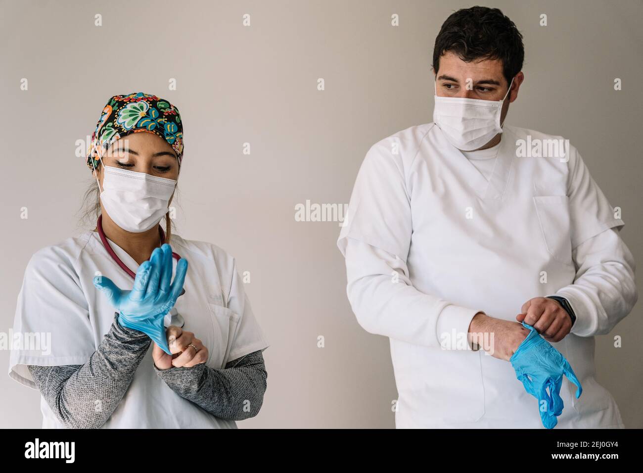 Male and female doctors in medical masks standing in hospital and putting on protective latex gloves while working during coronavirus pandemic Stock Photo