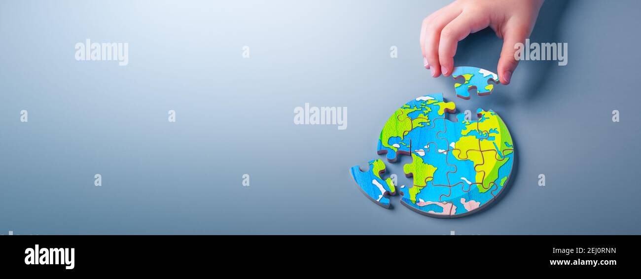 Close-up Of Child's Hand Solving Wooden Earth Puzzle On Soft Blue Background - Environmental Solutions Concept Stock Photo