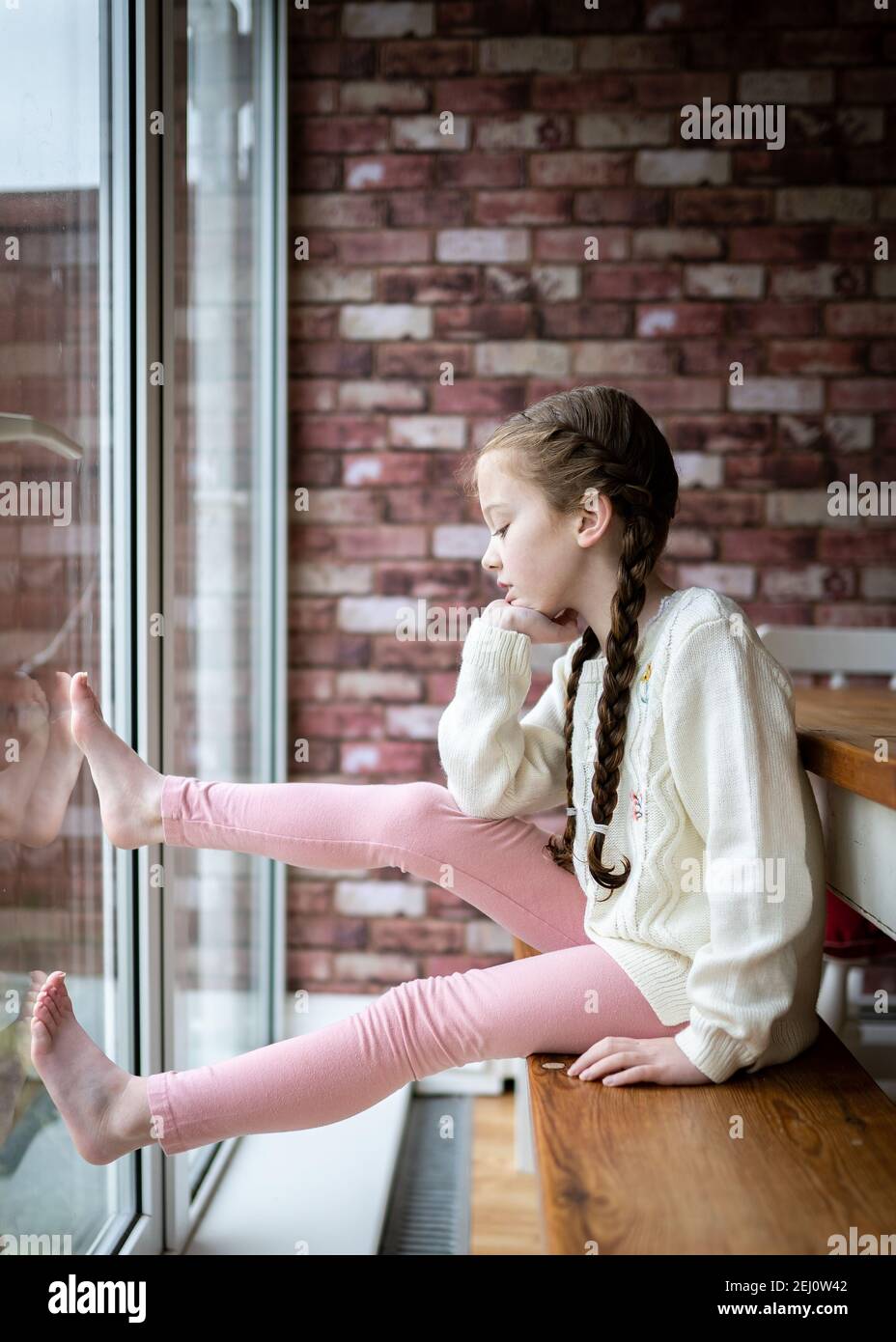 Young cute pretty girl with pigtails long hair stuck indoors sat at table looking at the ground outside sad bored head resting on hand  stuck indoors Stock Photo