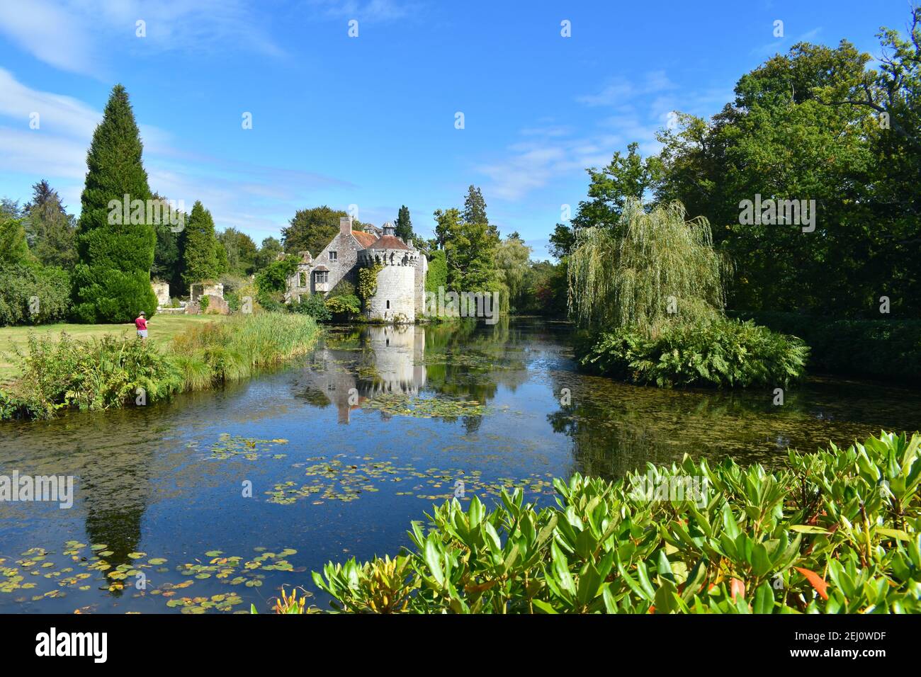 Woman drawing a medieval castle and its reflection in water Romantic gardens with panoramic views of a moated fortress and a Victorian country mansion Stock Photo