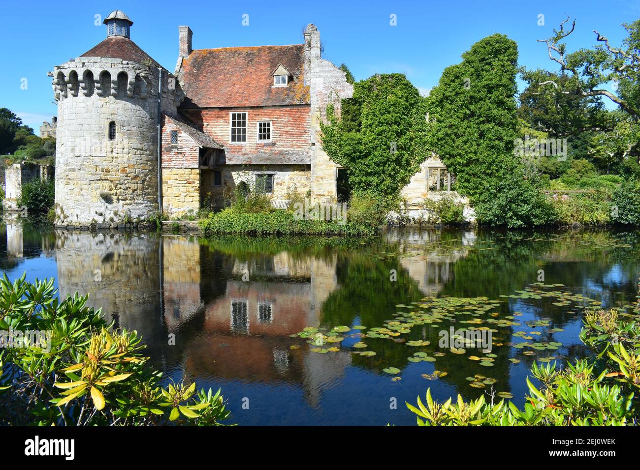 Centuries old British medieval castle facade amongst lush greenery with its reflection in water It includes tower residential buildings estates office Stock Photo