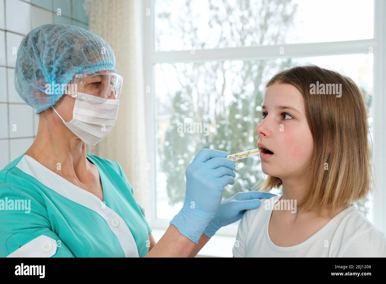 Doctor holds thermometer in mouth of young girl for measurement of temperature. Stock Photo
