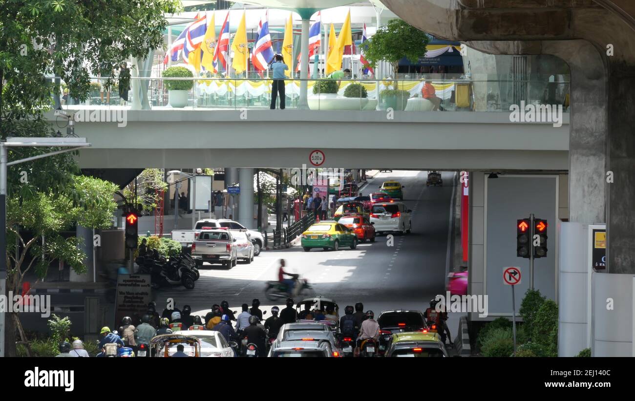 BANGKOK, THAILAND - 11 JULY, 2019: Intersection on busy city street. People on motorcycles and cars riding on crossroad under pedestrian bridge on bus Stock Photo