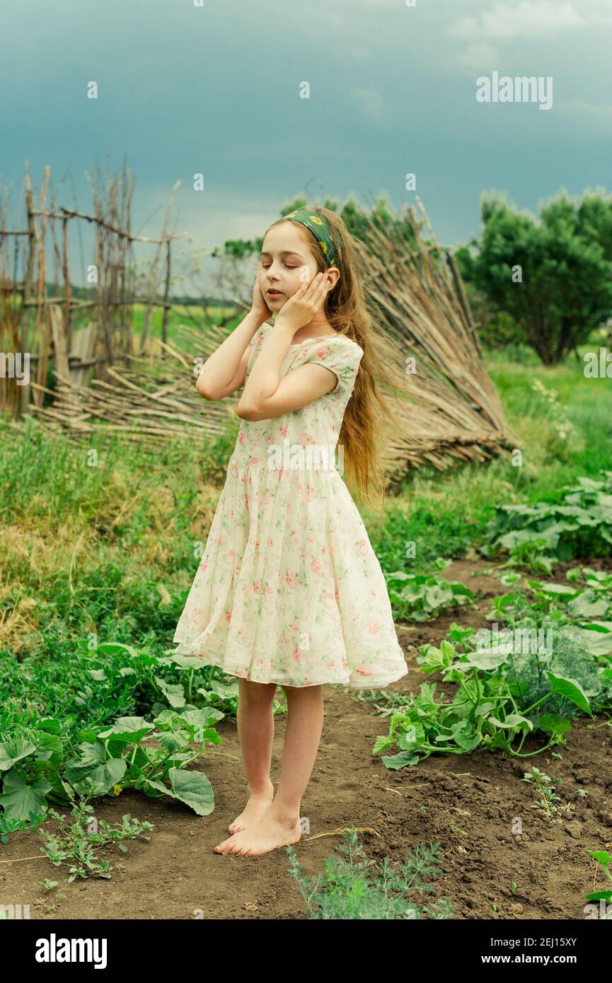 A little girl in a white dress with a flower stands barefoot in the ...