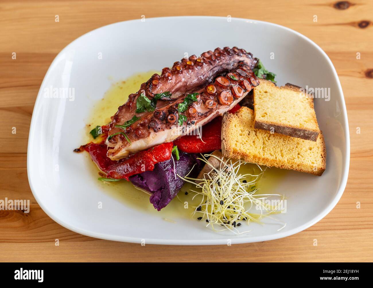 Simple but fancy looking plate of purple sweet potato, pepper and octopus legs with bread toast on the side. Stock Photo