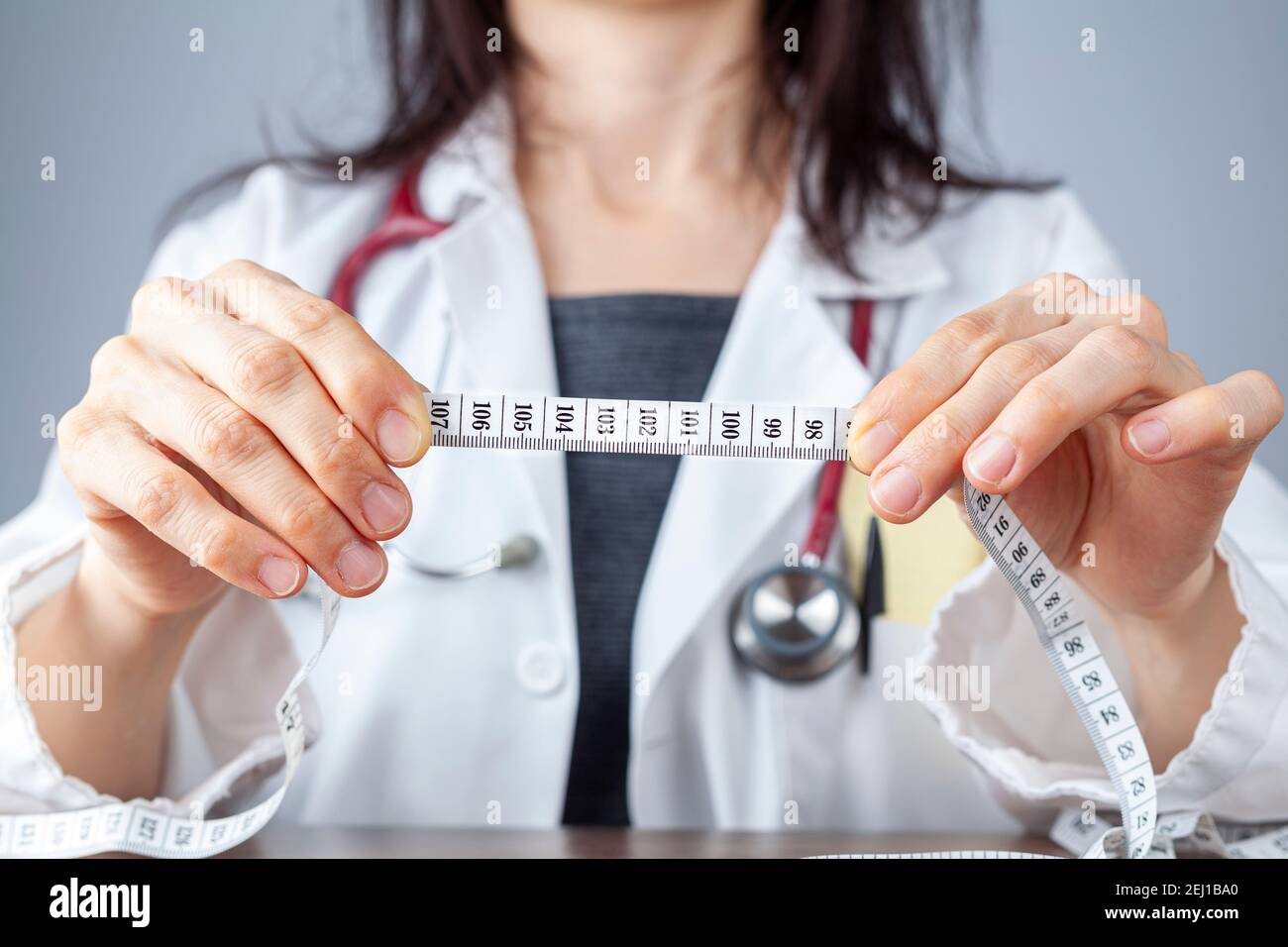 Close up isolated image of a caucasian doctor holding a tape measure in her hands showing 102 centimeters as abdominal circumference upper limit in he Stock Photo