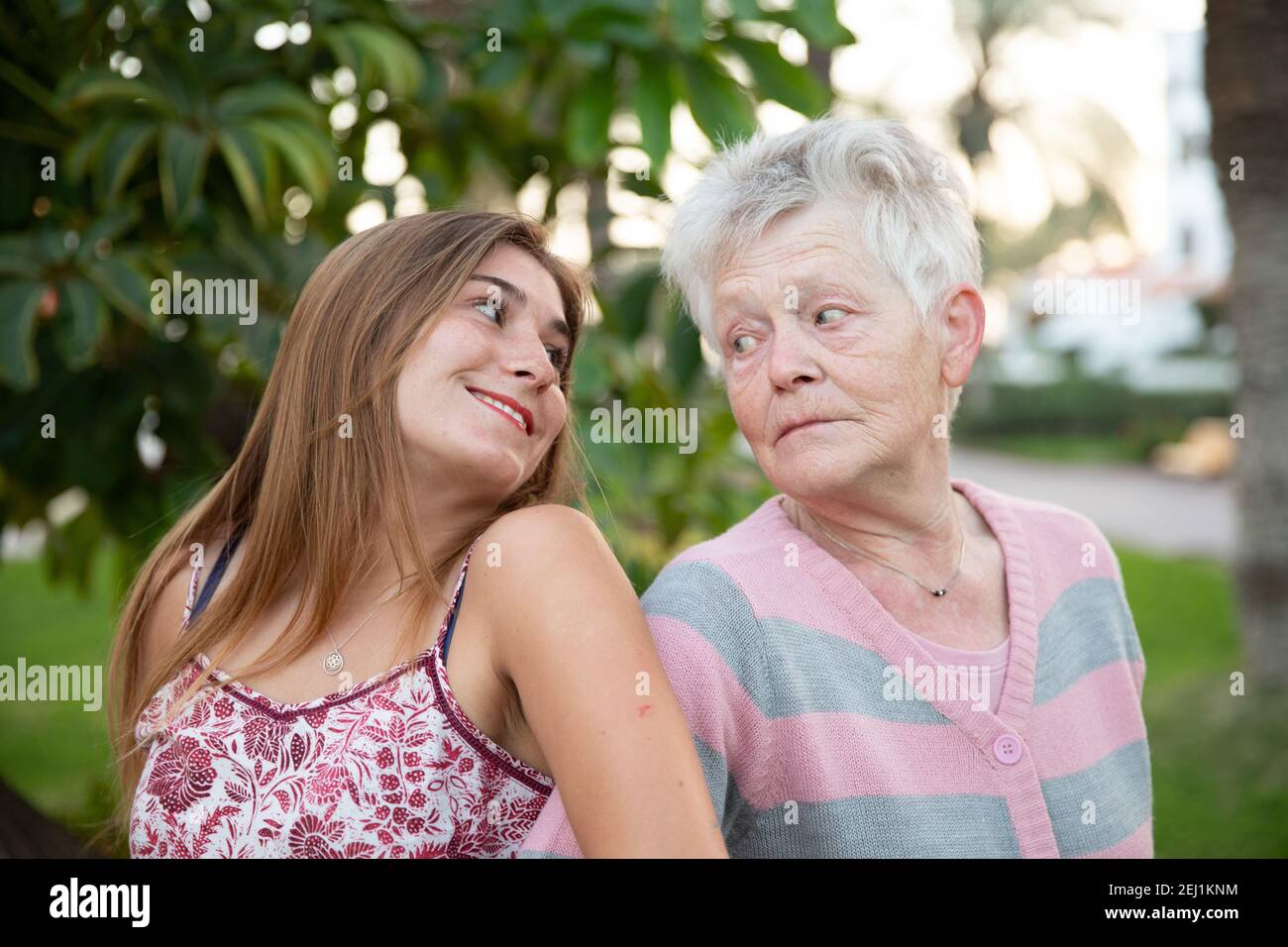 Grandmother and granddaughter stand back to back and smile at each other as they enjoy their holidays in an exotic location. Stock Photo