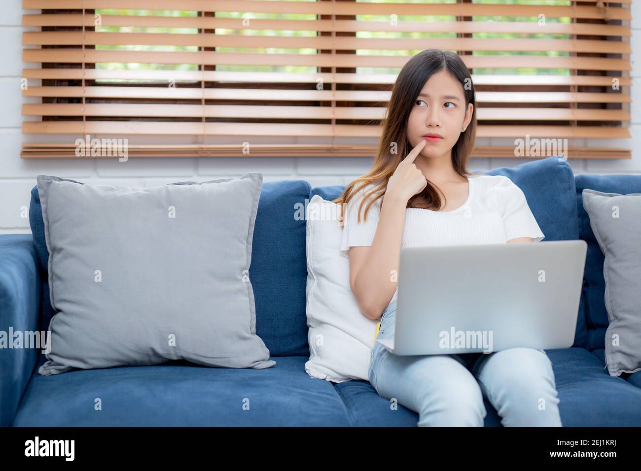 Beautiful young asian woman working on laptop computer and thinking ...
