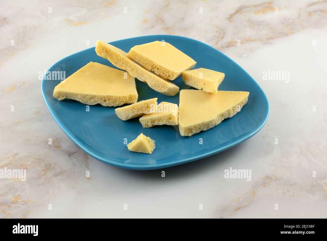 Broken caramel bubble white chocolate bar pieces on blue snack plate on table Stock Photo